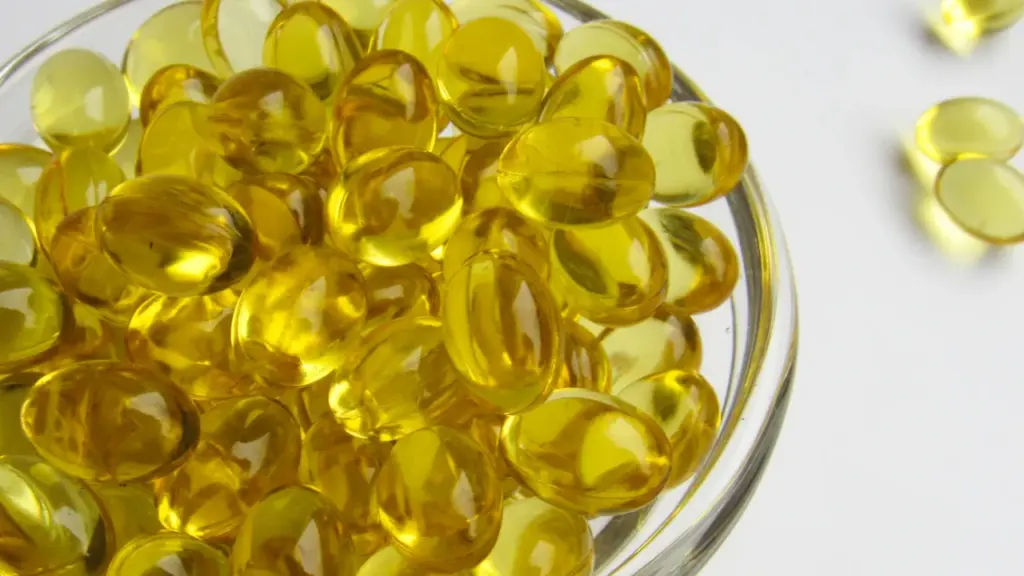 Dzeltenas D vitamīna kapsulas stikla traukā uz gaišas un tīras virsmas.