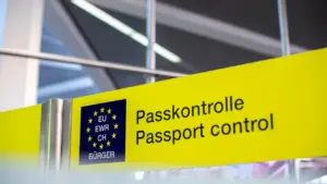Dzeltena norāde lidostā ar uzrakstu pasu kontrole un Eiropas Savienības simboliku.