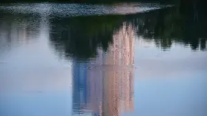 Ēkas atspulgs mierīgā ūdenī krēslas stundā, simbolizējot iekšējo līdzsvaru un sirdsmieru.