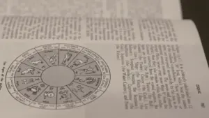 Atvērta grāmata ar zodiaka zīmju attēlojumu un detalizētu astroloģisku informāciju.