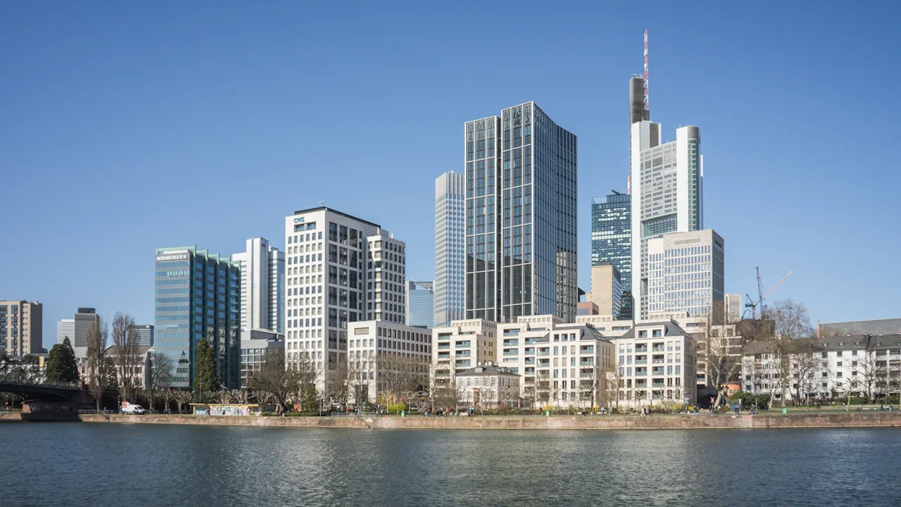 Frankfurtes debesskrāpji pie upes krasta, simbolizējot Eiropas centrālās bankas finanšu lēmumu ietekmi.