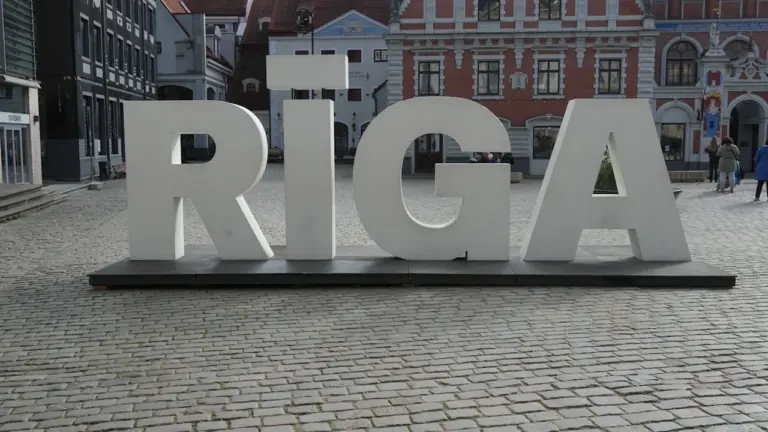 Liels, balts uzraksts RĪGA uz bruģēta laukuma Rīgas vēsturiskajā centrā.