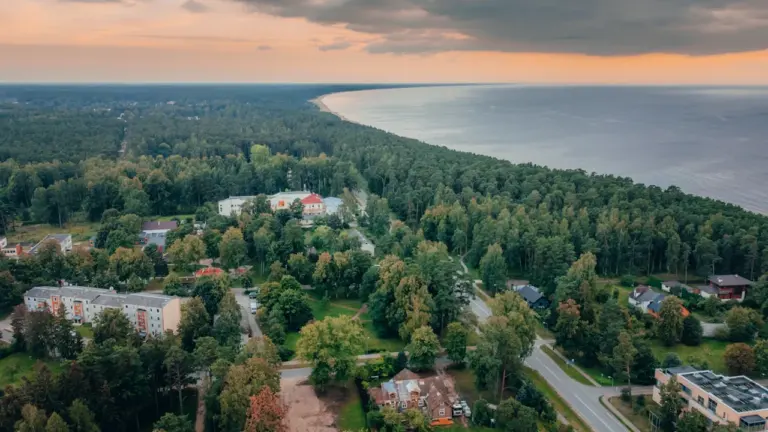 Latvijas piekrastes ainava ar mežu un jūru saulrietā, piemērota tūrisma stāstam.