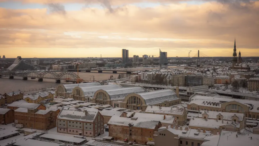 Panorāmas skats uz ziemīgu Rīgu ar sniegiem klātiem jumtiem saulrieta laikā.