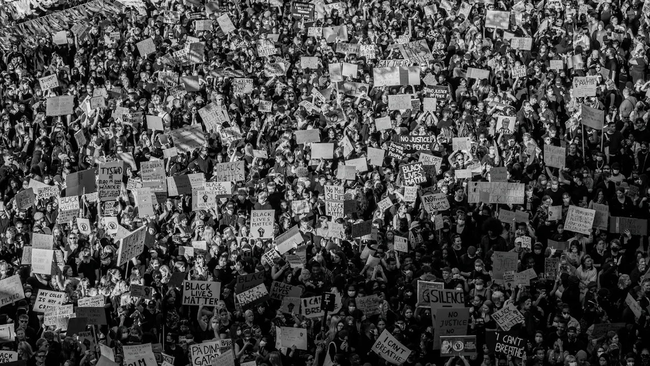 Cilvēku pūlis ar plakātiem piedalās pilsonisko tiesību protestā pilsētas ielās melnbaltā fotogrāfijā.