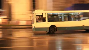 Steidzīgs autobuss brauc pa pilsētas ielu agrā rīta miglainā un zeltītā gaismā.